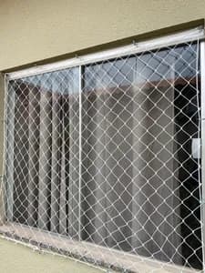 Rede de proteção branca fixada com ganchos em janela de alumínio residencial - UauTelas Terenos MS