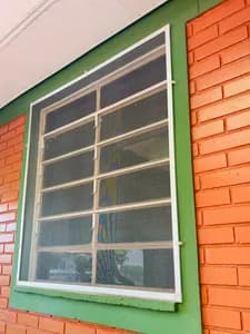 Tela mosquiteiro branca instalada externamente em janela com veneziana de vidro. - UauTelas Terenos MS