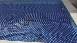 Detalhe de rede de proteção branca tensionada sobre piscina com pastilhas azuis no bairro Moreninha em Campo Grande MS